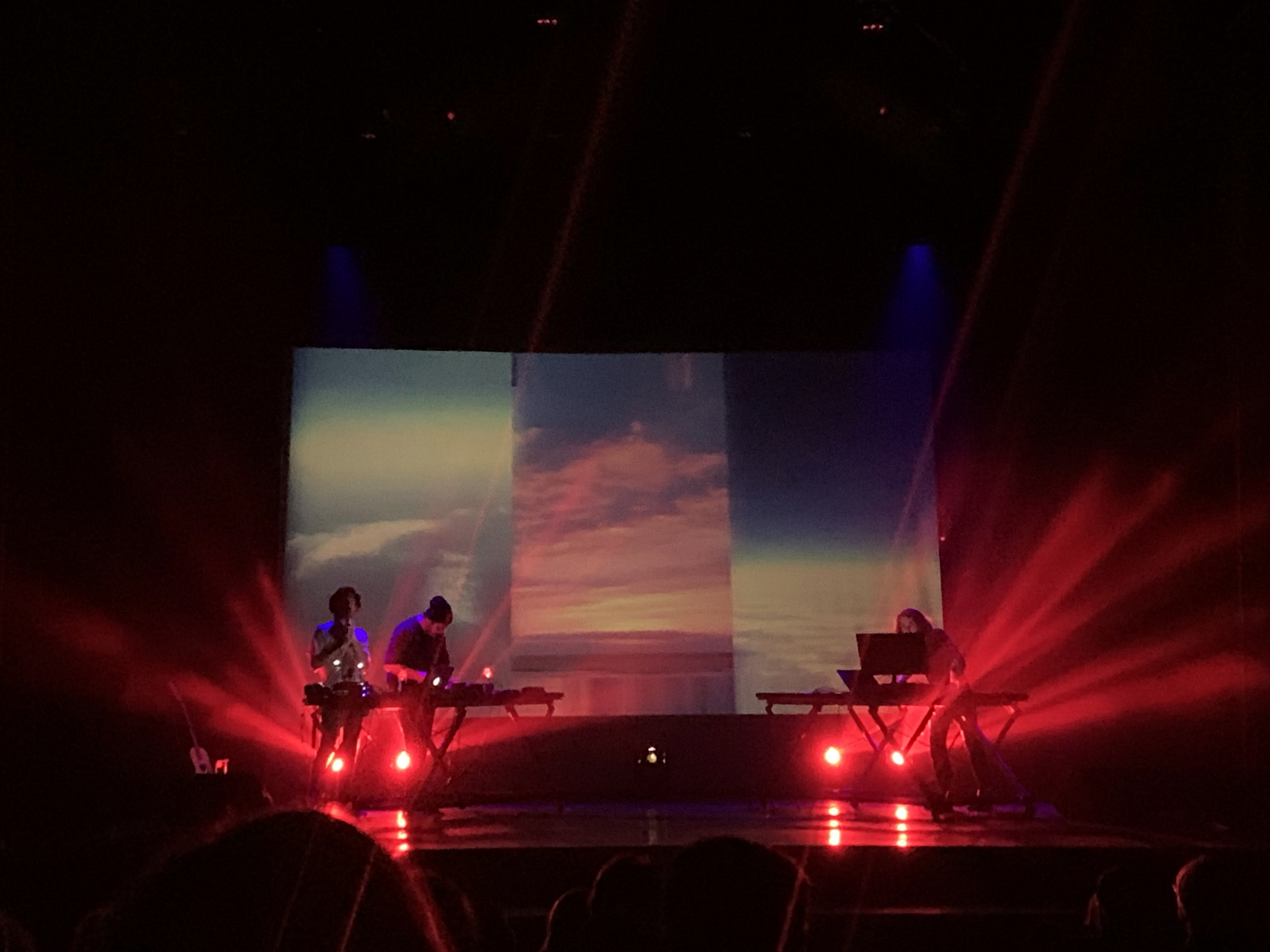 h0b0 in a band setting, performing live in front of a projection with footage of the sky and warm lights